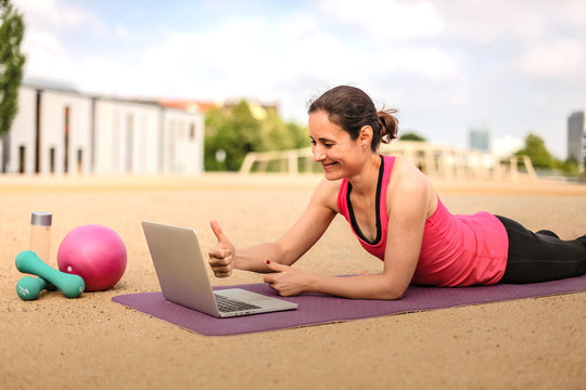 female fitness coach making  thumbs up infront of a laptop after an successful online workout  on a mat 