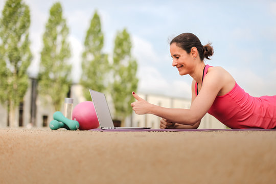 female fitness coach making  thumbs up infront of a laptop after an successful online workout  on a mat 