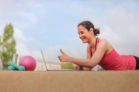 female fitness coach making  thumbs up infront of a laptop after an successful online workout  on a mat 