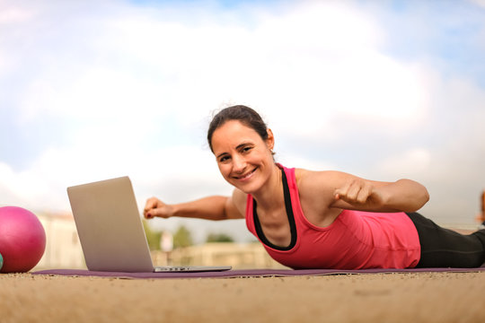 fit woman watching online fitness program and doing workout infront of a laptop on a mat