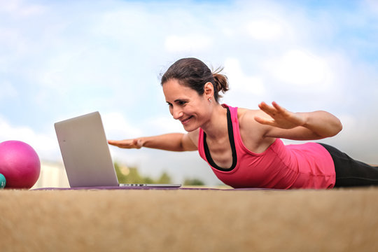 fit woman watching online fitness program and doing workout infront of a laptop on a mat