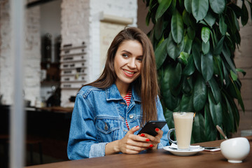 Young woman texting or using smartphone and drinking coffee