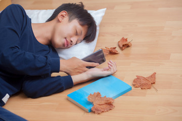 Happy boy sleep and holding phone his hands.Morning with brown dry leaf on the wooden floor in autamn season.
