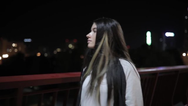 Young woman listening to music walking on a bridge at night time