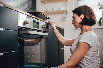 Woman using oven - obrazy, fototapety, plakaty