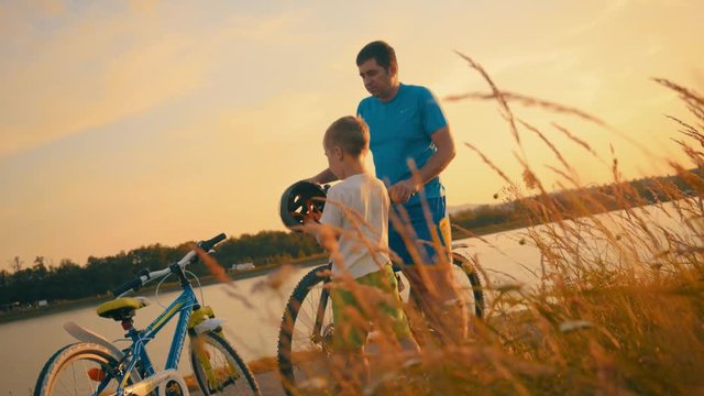 Happy Father and son cyclist rides on the road, river at sunset outdoors background,