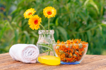 Towel, soap with marigold extract, calendula flowers in a glass jar and bowl with dry flowers of calendula