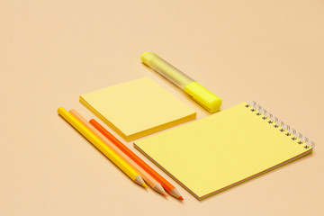 Color pencils, notebook, note-paper and yellow felt-tip pen on beige background