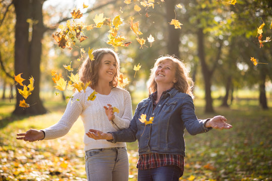 Having fun together - mother and daughter throwing autumn leaves