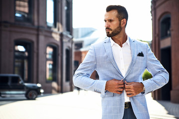 Portrait of sexy handsome fashion businessman model dressed in elegant blue suit posing on street background. Metrosexual