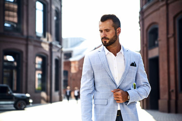 Portrait of sexy handsome fashion businessman model dressed in elegant blue suit posing on street background. Metrosexual