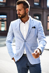 Portrait of sexy handsome fashion businessman model dressed in elegant blue suit posing on street background. Metrosexual