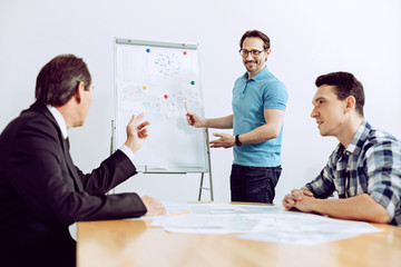 Clear information. Smiling calm positive worker explaining the diagram to his curious attentive colleagues