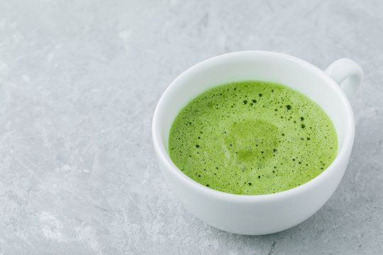 Japanese matcha green tea latte in white cup on gray background