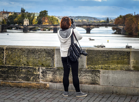 Prague, Czech Republic - October 10, 2017: Woman take photos and looks at Vltava river and bridges near Prague city center, Prague Czech Republic