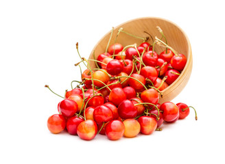 Cherries scattered from wooden bowl on white.
