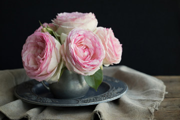 Vintage style photograph of a bouquet of pink Eden roses in a pewter vase on black