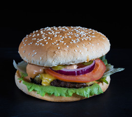 Burger with grilled meats, onions, tomatoes, lettuce, sauce and mustard, on a black background and a dark stone tray