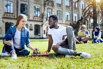 Favorite leisure activity. Radiant mates grinning broadly while sitting outdoors and enjoying a chess game together.