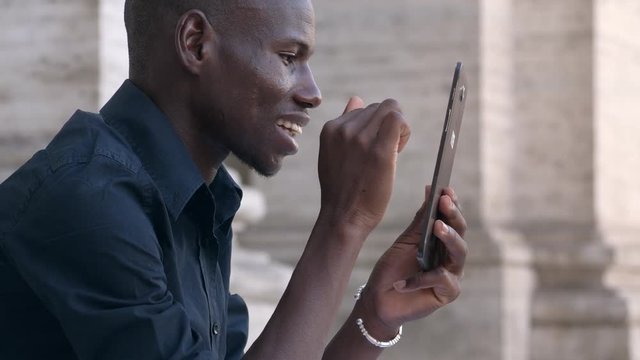 Happy american african young man scrolling his tablet smiling- outdoor