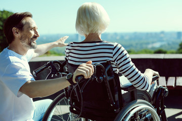 Have a look. Disabled woman sitting in her wheelchair and looking forward while spending time with volunteer