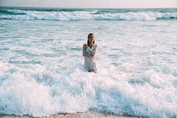The brunette in a beautiful suit is waist-deep in seawater, and white foam. The concept of relaxation, beach, bathing in the sea, sunbathing, people.