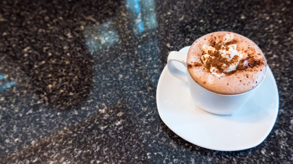 A cup of hot coffee is placed on a marble table. Reflecting the shadows of women who are watching the fashion fabric.