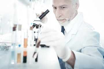 Biological research. Smart nice handsome biologist sitting in front of the microscope and taking a...
