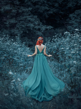 Red-haired girl in a blue, sapphire, luxurious dress in the floor, with an open back and a long train. The princess walks in a fairy forest. Photo from the back without a face. Artistic retouching