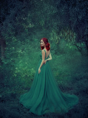 Red-haired girl in a green, emerald, luxurious dress in the floor, with an open back and a long...