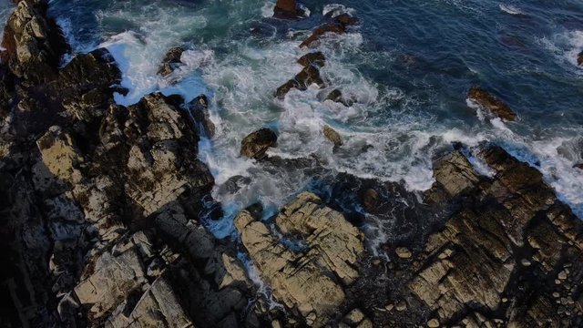 A top down view of the rocky New England coastline, tilting up to reveal the open ocean.  	