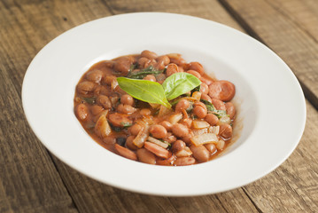 Cooked Red Beans in Tomato Sauce with Spinach and Onion, white Round Plate, Wooden Background, Top view.