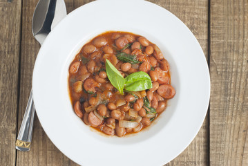 Cooked Red Beans in Tomato Sauce with Spinach and Onion, white Round Plate, Wooden Background, Top view.