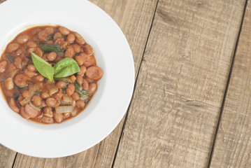 Cooked Red Beans in Tomato Sauce with Spinach and Onion, white Round Plate, Wooden Background, Top view, Copy space.