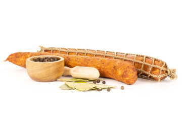 Group of two whole dry smoked ham sausage with bay leaves and pepper in a wooden bowl isolated on white