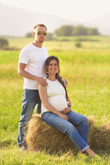 Young pregnant woman with her husband enjoying the nature wearing casual and style jeans and white t-shirt.