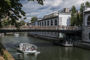 Naklejka premium Slovenia, 24/06/2018: lo skyline del centro di Lubiana con una barca turistica che naviga sul fiume Ljubljanica sotto il ponte dei macellai