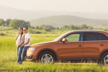 Young pregnant woman with her husband enjoying the nature. Traveling on family car in the field.