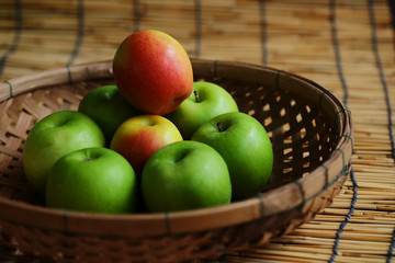 Set of green apple surround red apple in wood basket on wood mat and have some space for write wording, trendy delicious fruit for health concern people especially for weight control women or men