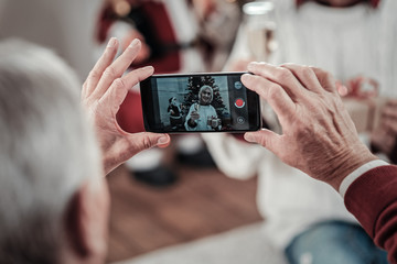 Lets celebrate. Grey-haired man using his camera while making photo of his wife, having New Year party
