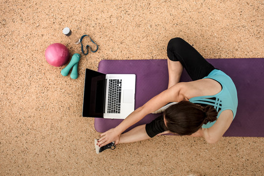 slim woman  stretching with Thera band infront of a laptop while watching online Fitness program on a yoga mat
