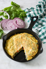 Frittata made of eggs and vegetables in a iron pan, on white marble