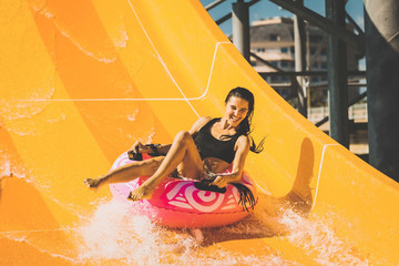 pretty smiling woman on the rubber ring having fun on the orange water slide in the aqua park....