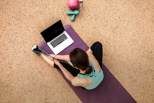 slim woman  stretching with Thera band infront of a laptop while watching online Fitness program on a yoga mat