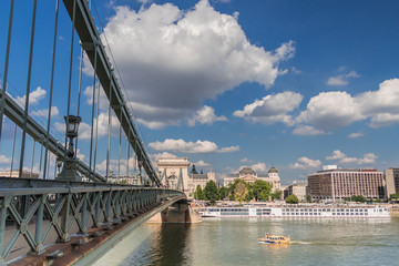 Fototapeta premium Budapest cityscape with the Chain Bridge across the Danube and ships sailing on the river. Row of buildings on the embankment under the blue cloudy sky on a sunny day.