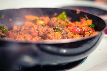 A pan of pasta sauce including peppers, sausage, carrots, kale, and assorted spices.