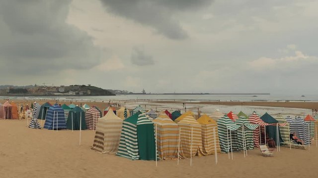 4 k Time-Laps frame posterise fasted video with view of Cnatabrian Sea beach with tent town, resting people, speedy moving clouds, orange-brown sand, moving and laying people at the summer cloudy warm