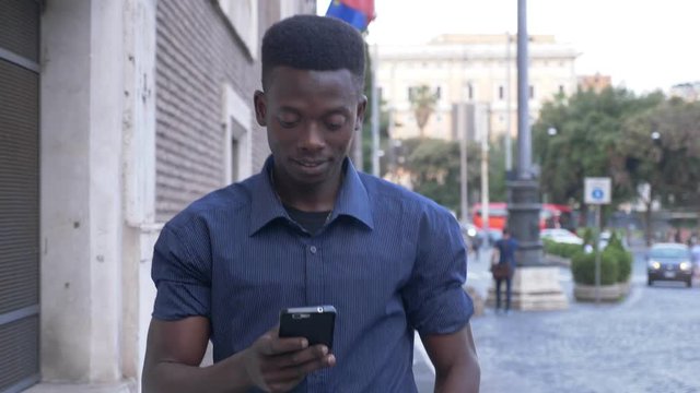 attractive black african man walking in the city, typing on his smartphone