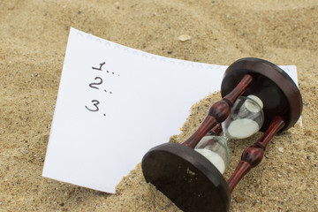 An hourglass and a list buried in the sand.