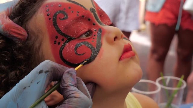 Young girl is getting face painted. A red ladybug/butterfly